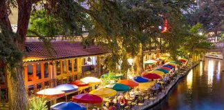 Outdoor riverside restaurant with colorful umbrellas and evening lights.