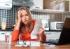 Woman looking stressed holding bills in kitchen