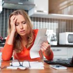 Illinois Families SLAMMED With Insane Bills Woman looking stressed holding bills in kitchen