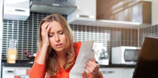 Woman looking stressed holding bills in kitchen