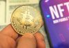 Person holding Bitcoin coin, NFT text on screen.