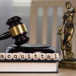 A gavel and the word acquittal spelled with letter blocks on a desk