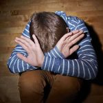 A child sitting on the floor with their hands covering their face, expressing distress