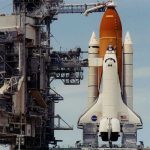 Space shuttle on launch pad with support structure.