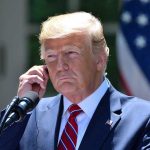 Trump’s Decisive Military Victory Stuns Democrats Man in a suit adjusting an earpiece.