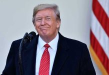 Trump TERMINATES Climate Science Man in suit and tie speaking at podium.