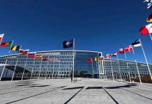 Flags outside NATO headquarters building under clear blue sky.
