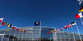 Flags outside NATO headquarters building under clear blue sky.