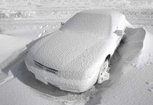 A car completely covered in snow, surrounded by a winter landscape