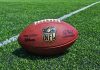 An NFL football resting on a green grass field