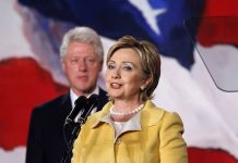 Hillary Clinton delivering a speech with Bill Clinton in the background