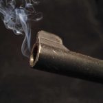 Close-up of a gun barrel emitting smoke against a black background