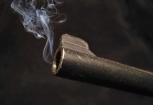 Close-up of a gun barrel emitting smoke against a black background