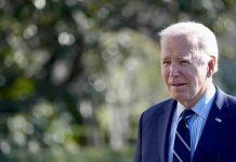 Man in a suit standing outdoors, blurry background.