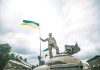 Ukraine Strikes Trigger SHOCKING Border Threat Soldier on tank holding Ukrainian flag.