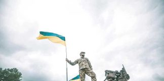 Soldier on tank holding Ukrainian flag.