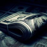 Trans Icon’s $115K COVID-19 Relief Heist A rolled stack of hundred-dollar bills on a background of more banknotes