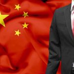 A man in a suit stands in front of the Chinese flag