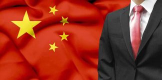 A man in a suit stands in front of the Chinese flag