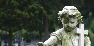 Weathered statue of a child angel holding a cross in a cemetery