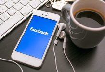 Smartphone displaying Facebook logo next to a cup of coffee and earphones