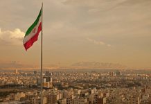 Iran’s Regime Surviving Massive Uprising Iranian flag waving over a city skyline with mountains in the background