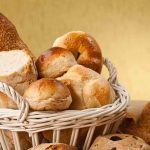 Fatal Dough Machine TRAPS Veteran Baker A basket filled with various types of fresh bread and rolls against a golden background