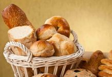 A basket filled with various types of fresh bread and rolls against a golden background