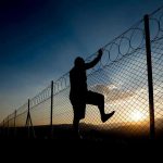 Child Monster Freed by Parole Board in California Silhouette of person climbing barbed wire fence at sunset.