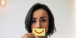 Woman holding smiley face card over mouth