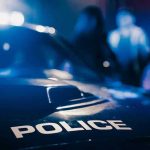 WNBA Star ARRESTED After Title Night Police car with blurred figures in the background.