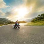 Route 66’s 100th Birthday Sparks Nationwide Revival Person rides motorcycle on curved mountain road at sunset.