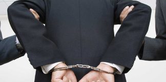 A person in a suit with hands cuffed behind their back