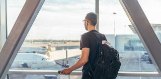 A traveler looking out of an airport window at parked airplanes