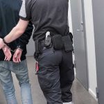 Officer escorting handcuffed person down hallway.