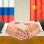 Two hands shaking in front of two flags.