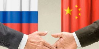 Two hands shaking in front of two flags.