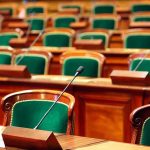 Empty legislative chamber with green upholstered chairs and wooden desks