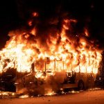 A bus engulfed in flames at night, with smoke billowing into the air