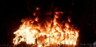 A bus engulfed in flames at night, with smoke billowing into the air