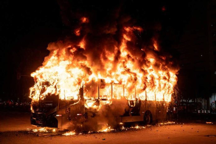 1439078420 A bus engulfed in flames at night, with smoke billowing into the air