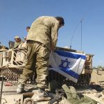 Soldier placing Israeli flag on military vehicle.