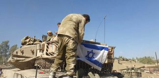 Soldier placing Israeli flag on military vehicle.