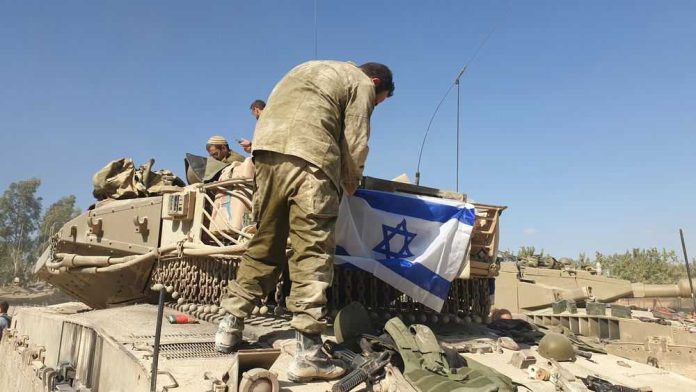 Soldier placing Israeli flag on military vehicle.