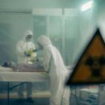 Two scientists examining a patient with biohazard sign visible.
