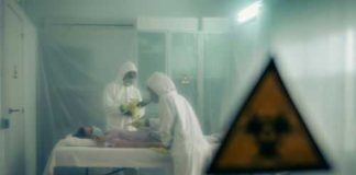 Two scientists examining a patient with biohazard sign visible.