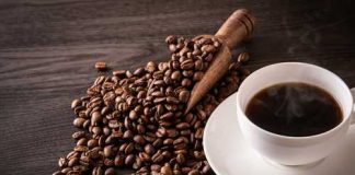 A cup of hot coffee next to spilled coffee beans and a wooden scoop
