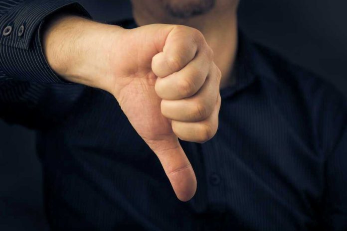 Hand showing thumbs down gesture, dark background.