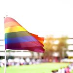 Rainbow flag waving in the foreground with a blurred crowd in the background