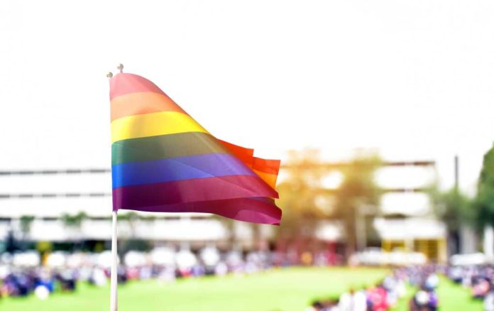 shutterstock_2132683097 Rainbow flag waving in the foreground with a blurred crowd in the background
